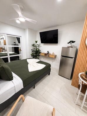 A modern bedroom with a bed, a desk, a television, a plant, and a refrigerator. - Private Las Vegas Studio + Kitchen + Separate Entrance (Las Vegas)