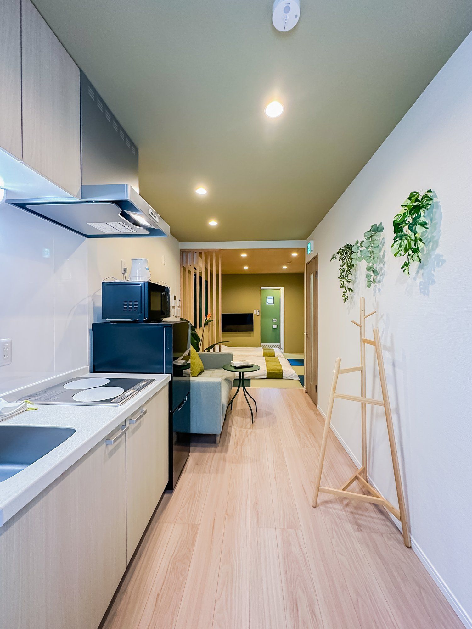 A modern kitchen with a built-in microwave, a coffee maker, and a sink. There is a wooden floor and a view of a living area with a sofa and a plant.