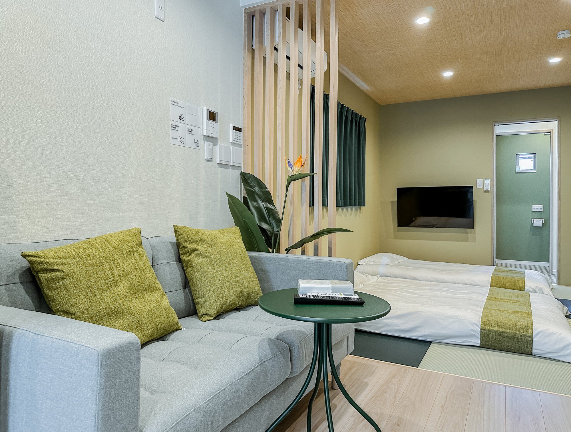 A hotel room with a sofa, a small round table, a bed with a TV, and a wooden partition.