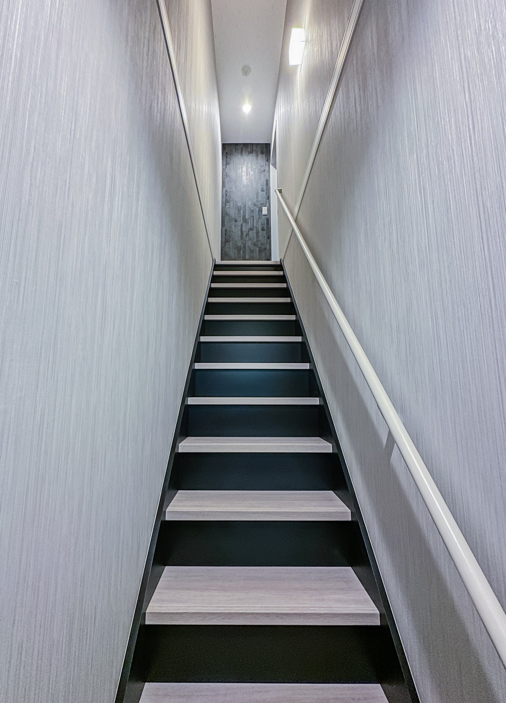 A modern staircase with a handrail, leading to a room with a patterned wall and a ceiling light.
