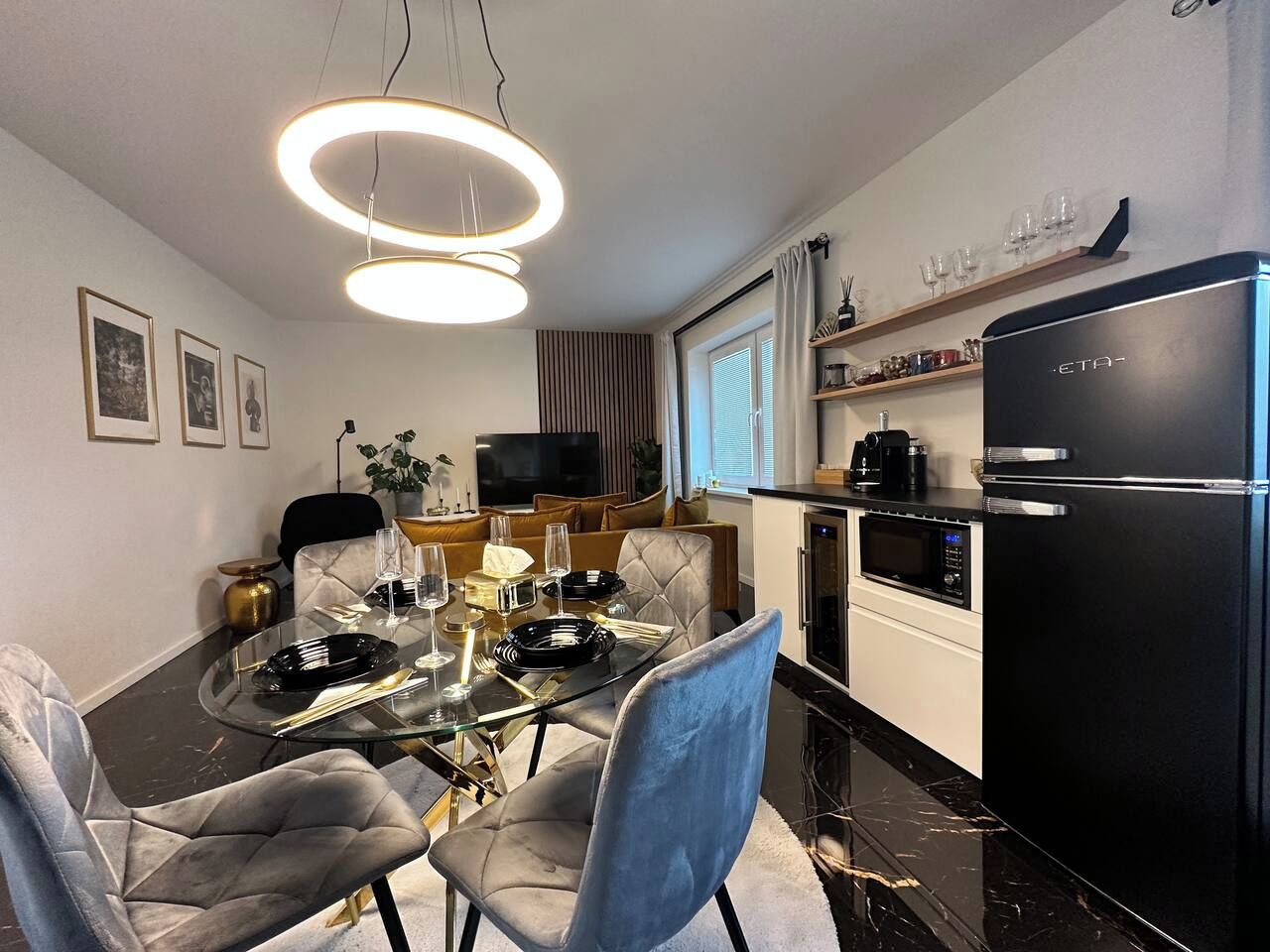 A modern kitchen with a black refrigerator, a dining table set with plates, and a television in the background.