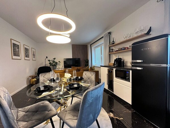 Una cocina moderna con un refrigerador negro, una mesa de comedor con platos y un televisor al fondo.