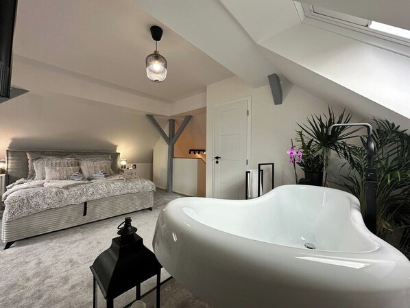 A bedroom with a large bed, a white bathtub, and a ceiling light.