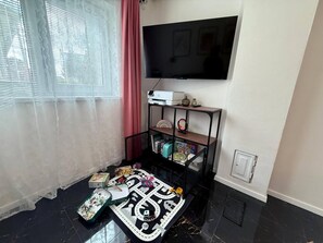 Un salon doté d’un téléviseur à écran plat fixé au mur, d’un meuble noir contenant divers objets, d’un tapis à motifs et d’une fenêtre ornée de rideaux légers.
