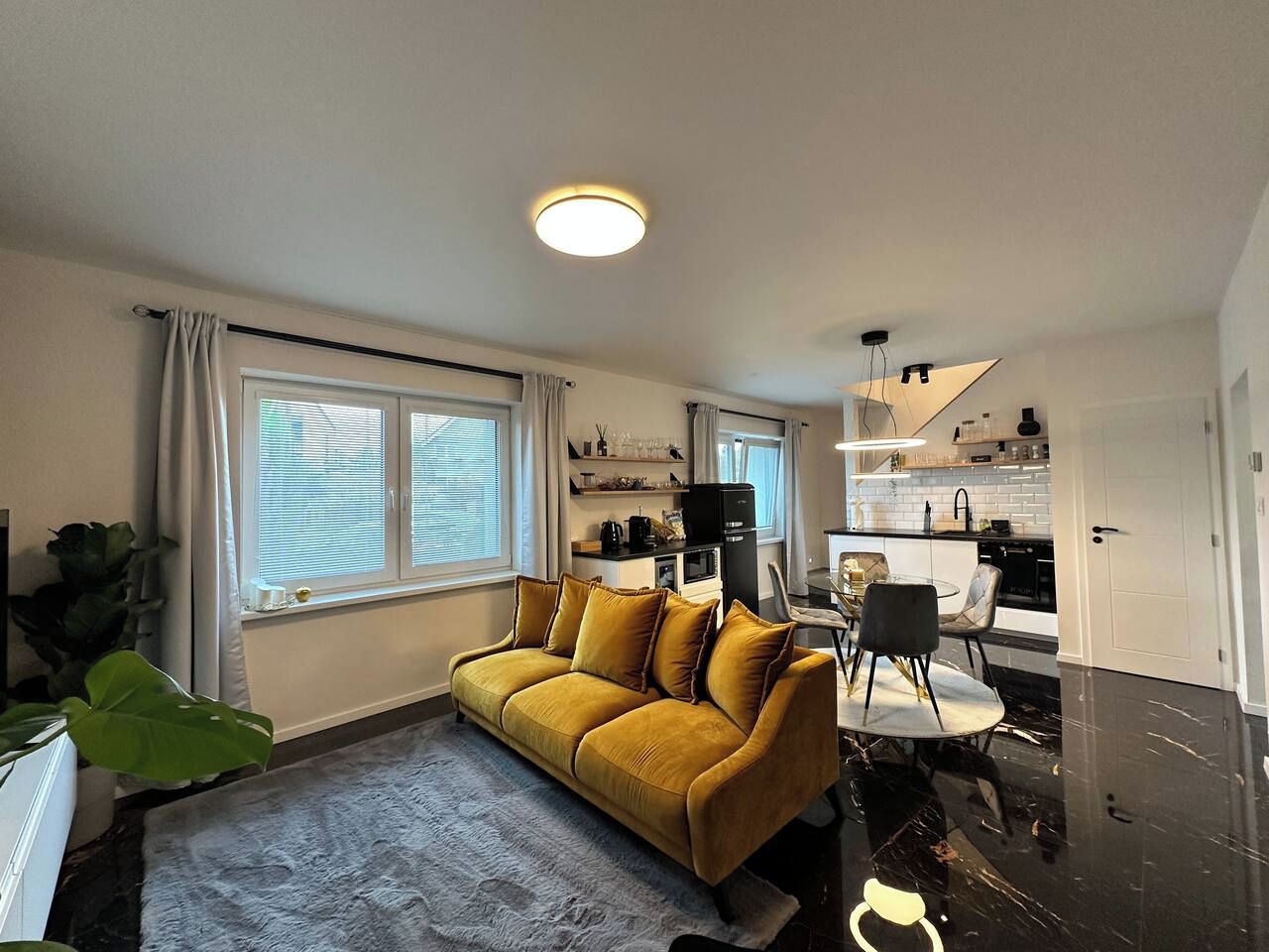 Un salon moderne comprenant un canapé, une table à manger avec des chaises, un coin cuisine et une grande fenêtre avec des rideaux.