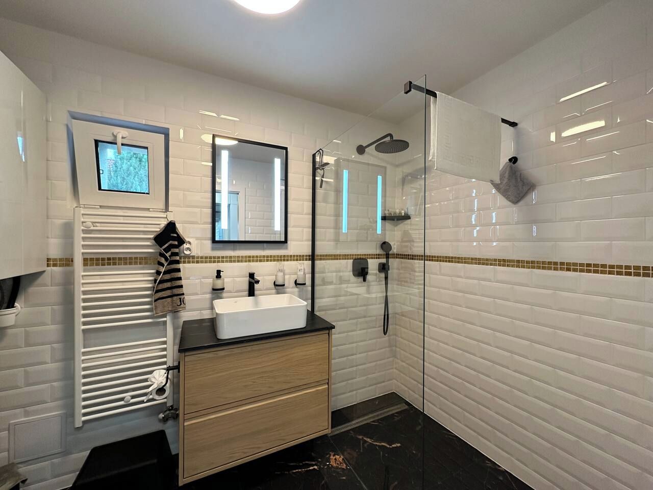 Ein modernes Badezimmer mit einer weißen Fliesenwand, einem rechteckigen Waschbecken, einem Spiegel, einer Duschkabine aus Glas und einem Handtuchhalter.