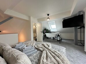 A bedroom with a large bed, a flat-screen TV, a skylight, and a bathtub.