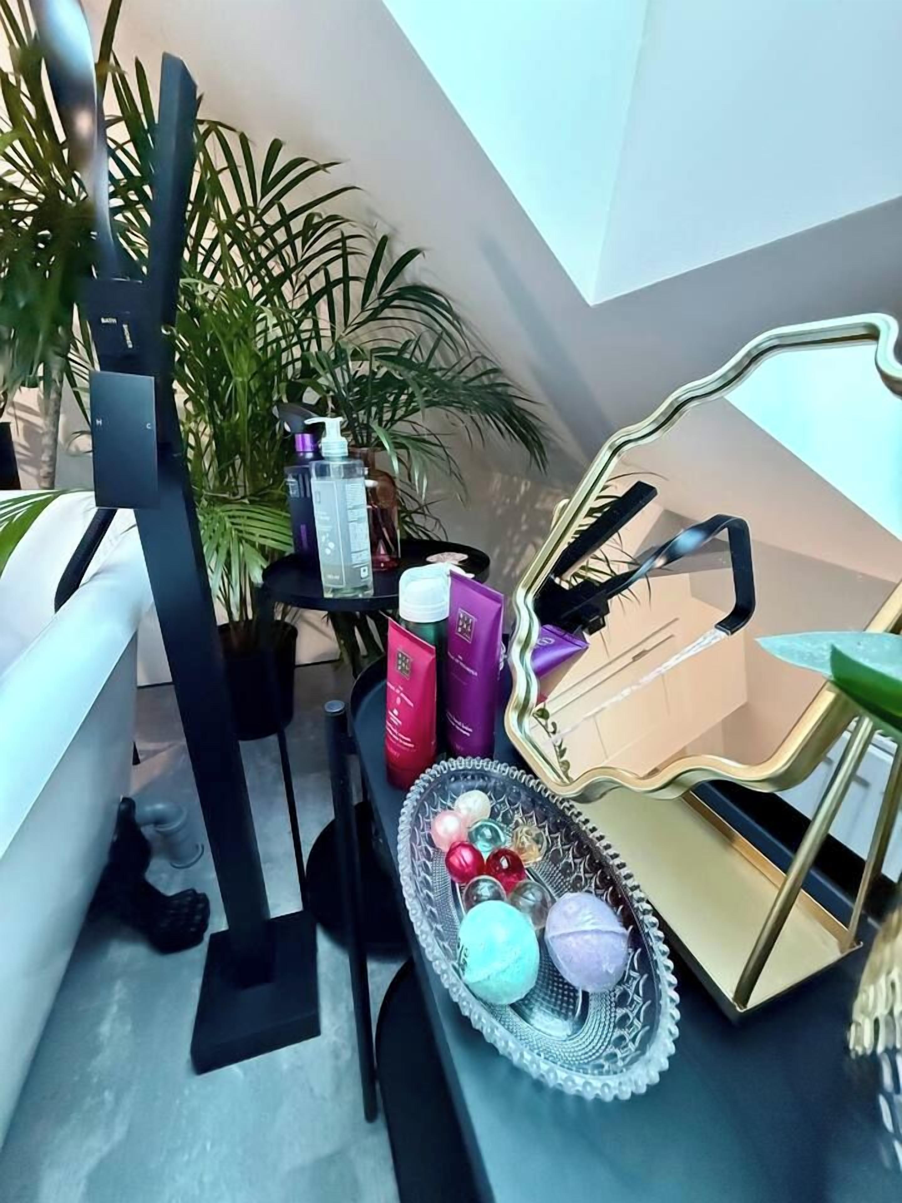 Une pièce comprenant un lit, un bureau avec un miroir, une plante en pot et une petite table sur laquelle se trouvent divers objets.