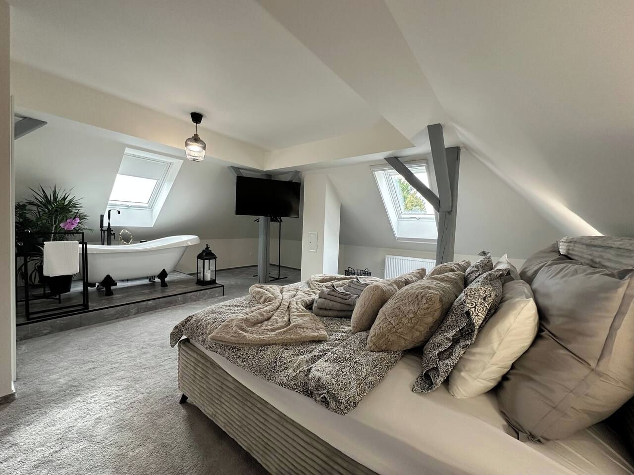 A bedroom with a large bed, a bathtub, and a skylight.