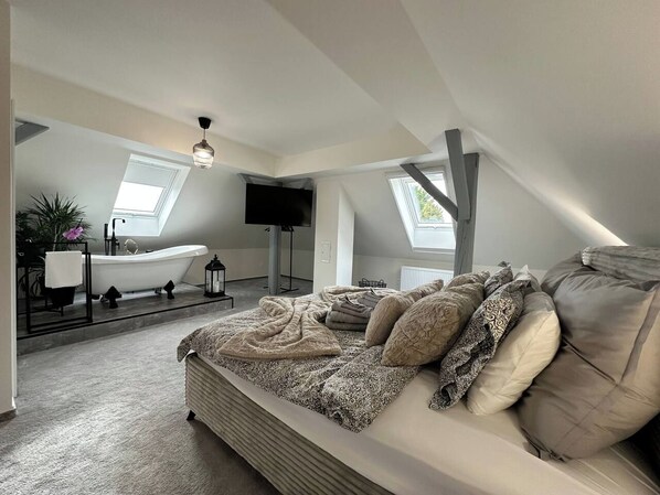 A bedroom with a large bed, a bathtub, and a skylight.