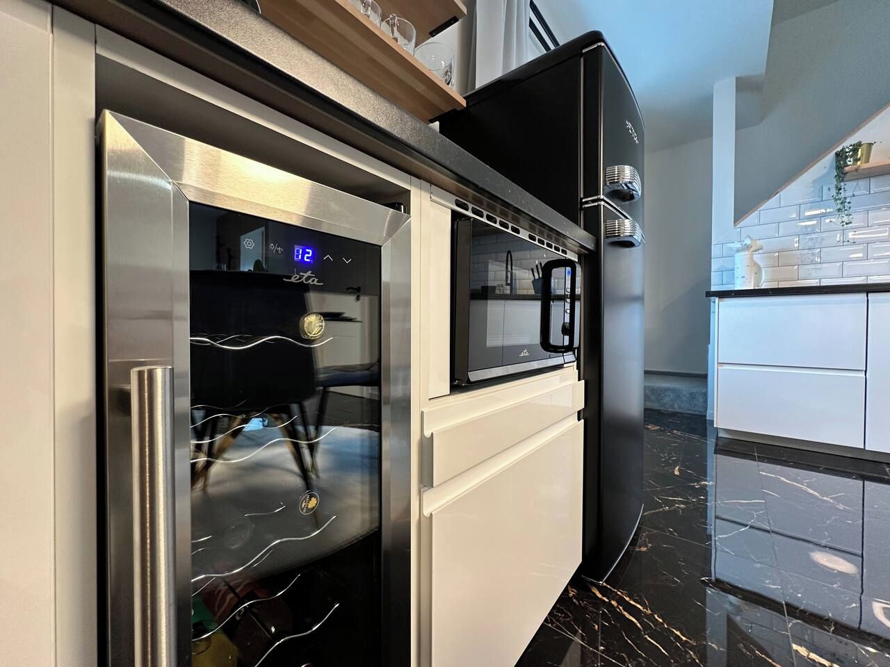 Una cocina moderna con horno empotrado y microondas, refrigerador de acero inoxidable y encimera de mármol.