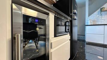 Una cocina moderna con horno empotrado y microondas, refrigerador de acero inoxidable y encimera de mármol.