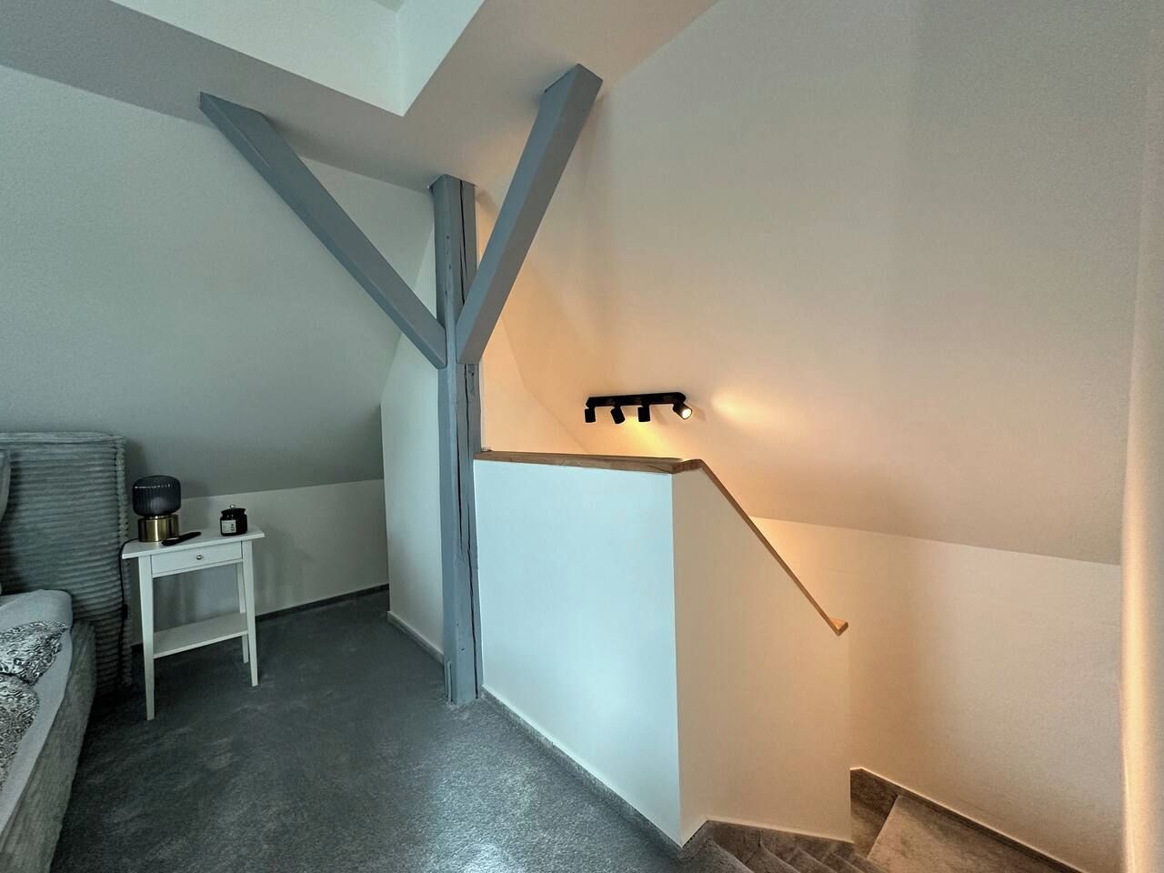 Een kamer met een bed, een klein nachtkastje met lamp en een wandplank met verlichting.
