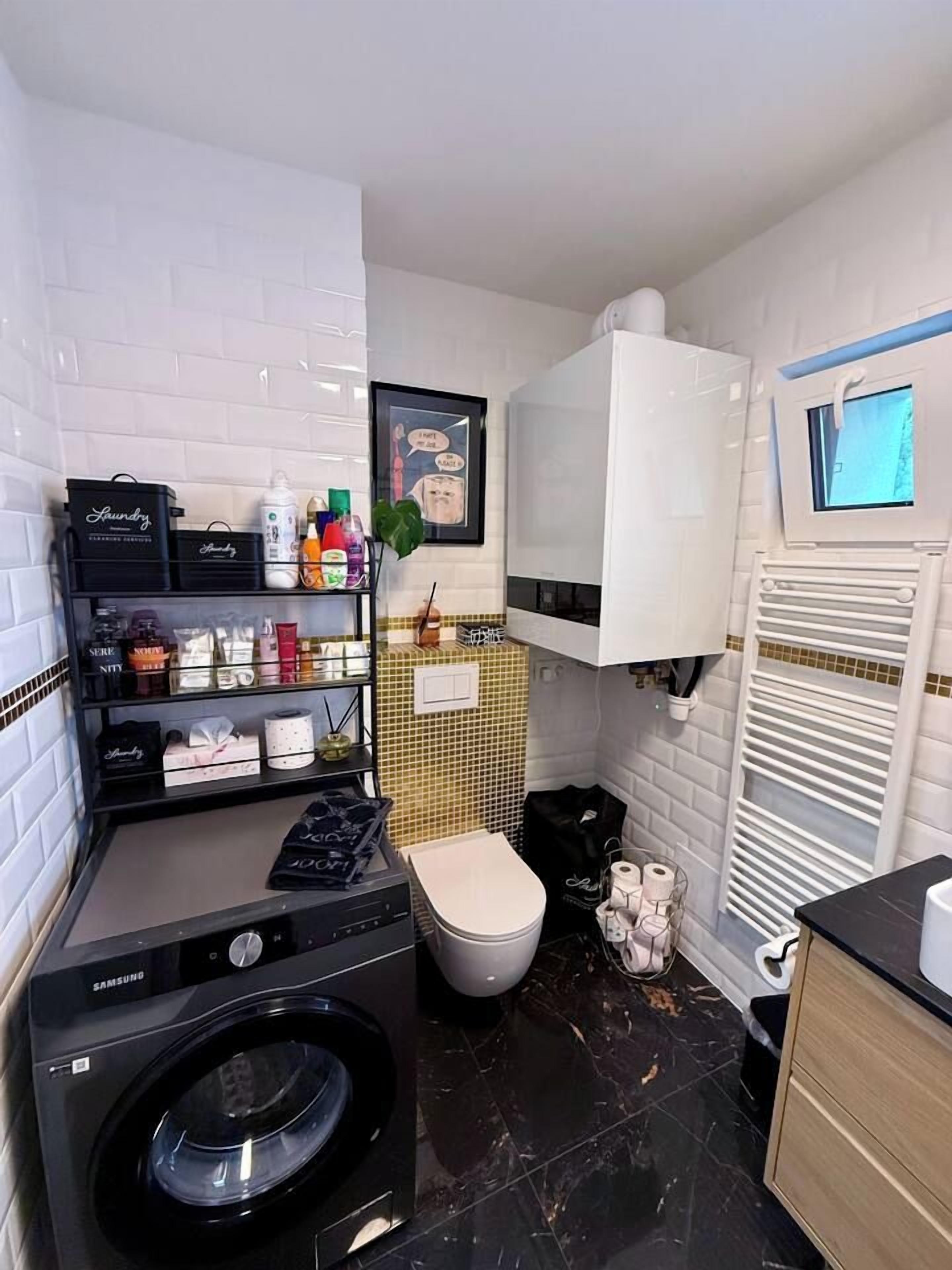 Een kleine badkamer met een wasmachine, toilet en een plank met toiletartikelen.