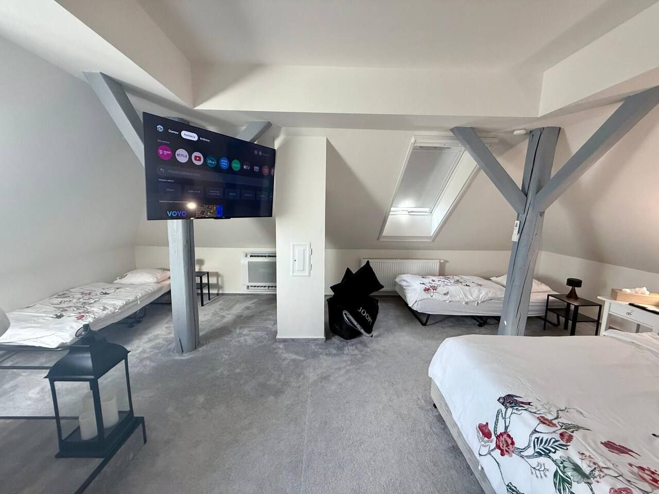 Quarto com duas camas, televisão na parede e uma mesinha.