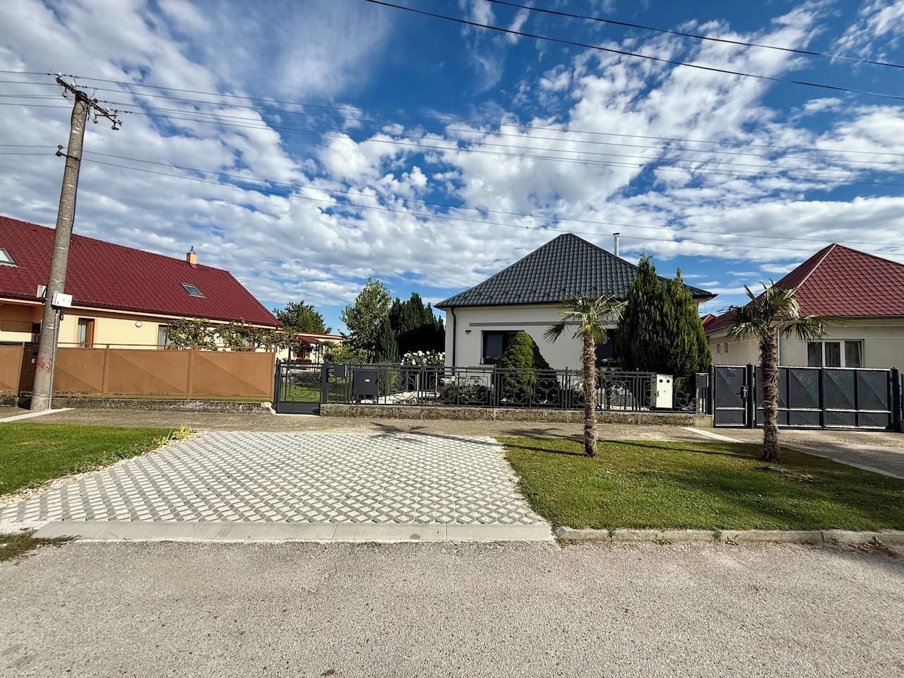 A residential area with a paved driveway, a house with a red roof, and a gated entrance.