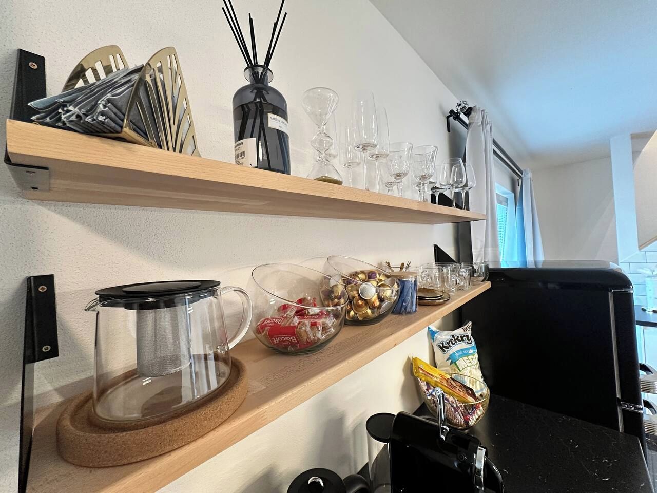 A kitchen with shelves holding kitchenware, a coffee maker, and a bag of chips.