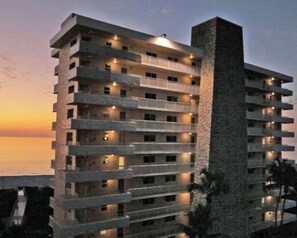 Ein mehrstöckiges Hotel mit Balkonen, einem zentralen Turm und Blick auf das Meer im Abenddämmerung.