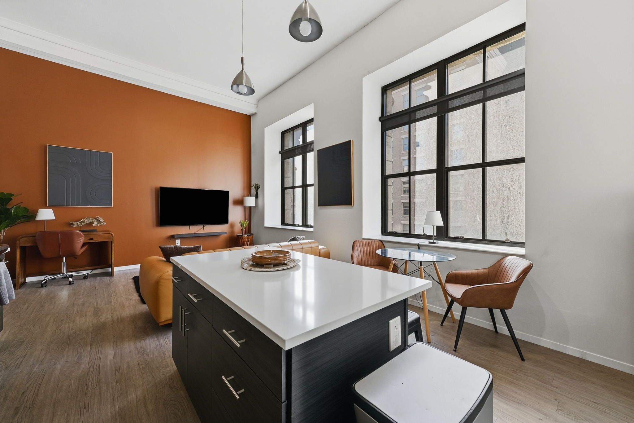A modern living room with a large window, a flat-screen TV, and a dining area with a round table.