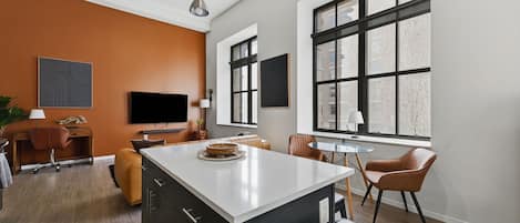 A modern living room with a large window, a flat-screen TV, and a dining area with a round table.