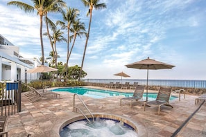 A pool area with lounge chairs and umbrellas, surrounded by palm trees and a view of the ocean. - Royal Sea Cliff 2BR Resort Suite Kona Coast (Kailua-Kona)