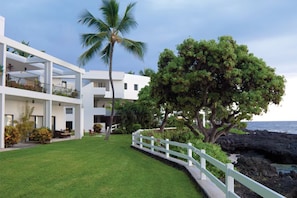 A modern hotel with a white exterior, a well-maintained lawn, a white fence, and a large tree. - Royal Sea Cliff 2BR Resort Suite Kona Coast (Kailua-Kona)