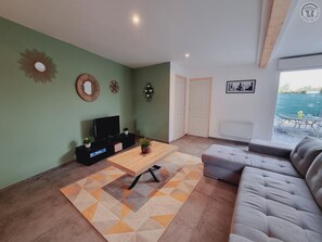 A modern living room with a sofa, a coffee table, and a TV. There is a door leading to a balcony with a view. - House with pets allowed - 6 guests (Hasnon)