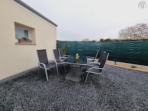 An outdoor patio with a table and chairs, a window with a plant, and a green fence. - House with pets allowed - 6 guests (Hasnon)