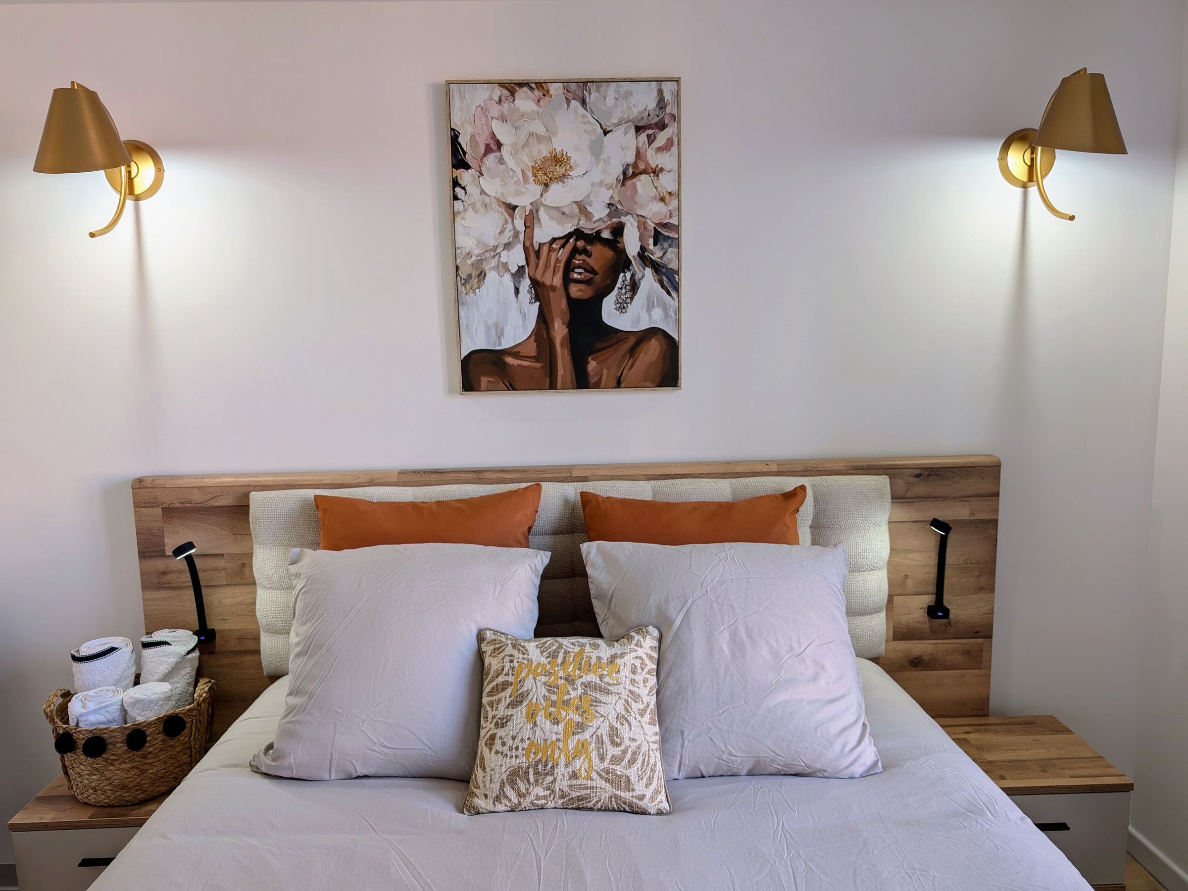 A bed with white bedding, two pillows, a decorative pillow, and a basket of towels on a wooden nightstand.