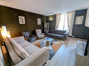 A modern living room with a sofa, armchairs, a coffee table, and a television. - Chic apartment in Luxeuil-les-Bains - 4 guests (Luxeuil-les-Bains)