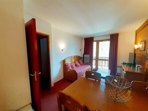 A hotel room with a bed, a desk, a chair, a television, and a balcony with curtains. - Apartment with park view – 6 guests (Valfréjus)