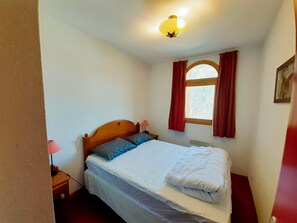 Un dormitori amb un llit individual, una tauleta de nit, una làmpada, una finestra amb cortines i una làmpada de paret.