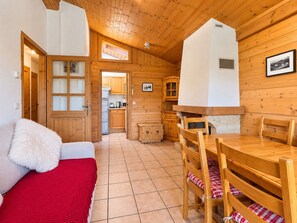 A cozy room with a wooden ceiling, a dining area with a table and chairs, a kitchen with wooden cabinets, and a red blanket on a bed. - Apartment facing Mont Charvin (Notre-Dame-de-Bellecombe)