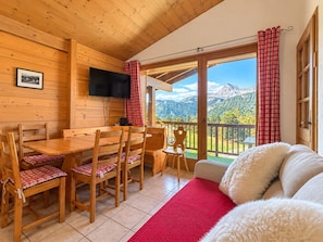 A wooden interior with a dining area, a flat-screen TV, and a balcony with a mountain view. - Apartment facing Mont Charvin (Notre-Dame-de-Bellecombe)