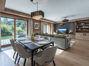 A modern living room with a dining area, wooden flooring, and large windows offering a view of the outdoors. - Spacious apartment near slopes - 6 guests (Megève)