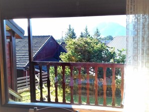 Ein Balkon mit Holzgeländer, Blick auf eine Wohngegend mit Häusern und Bäumen, und ein Berg im Hintergrund.