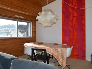 A dining area with a table, chairs, a view through a window, and a wall with a geometric pattern. - Cozy duplex, pets welcome - 8 guests (Bolquère-Pyrénées 2000)