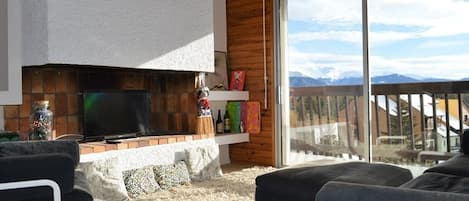 A living room with a fireplace, a television, and a view of mountains through a sliding glass door.