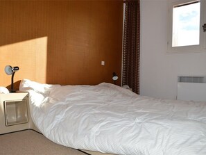 A hotel room with a bed, a desk, a chair, a window, and a radiator. - Cozy duplex, pets welcome - 8 guests (Bolquère-Pyrénées 2000)