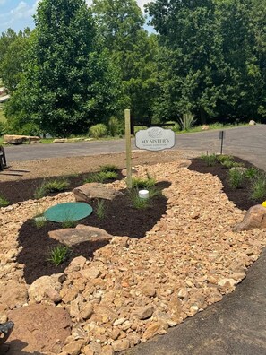 A sign for 'My Sister's Sewing Sanctuary' with a landscaped garden area featuring rocks, mulch, and a small pond. - Parkville Group Getaway - Sleeps 12 with 12 Individual Workstations (Parkville)