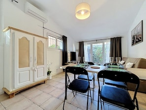 A well-lit room with a dining table, chairs, a sofa, a television, and a window with curtains. - Le Jasmin: Your cozy retreat in the heart of Provence (Trans-en-Provence)