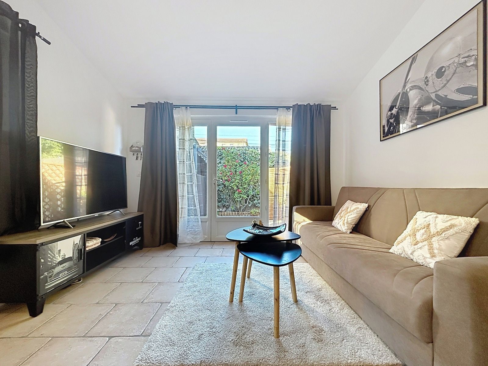 Un salon avec un téléviseur, un canapé, une petite table et une vue sur l’extérieur, visible à travers une porte vitrée.