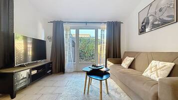 Un salon avec un téléviseur, un canapé, une petite table et une vue sur l’extérieur, visible à travers une porte vitrée.