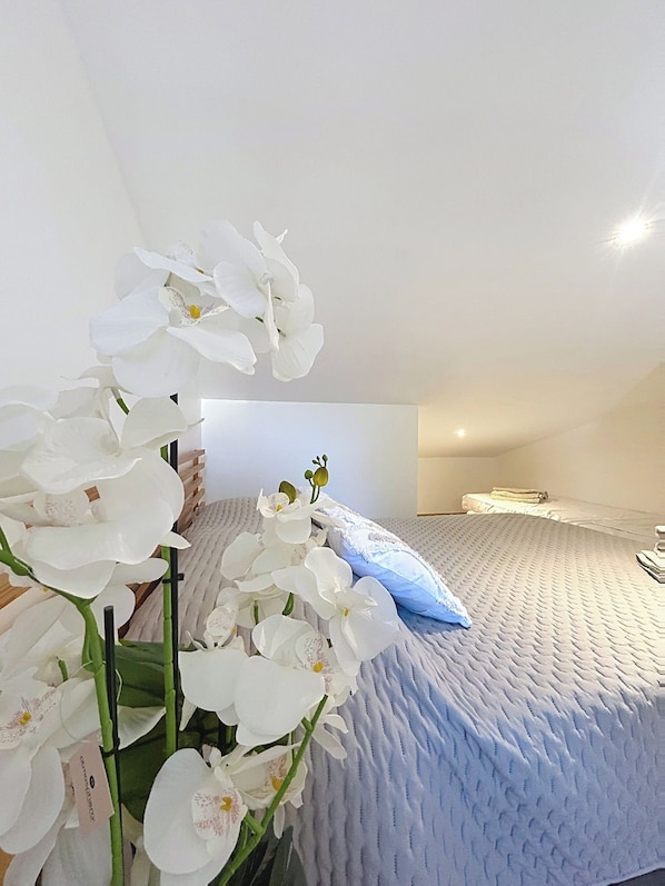 A bedroom with a bed, white orchid flowers, and a blue pillow. - Le Jasmin: Your cozy retreat in the heart of Provence (Trans-en-Provence)