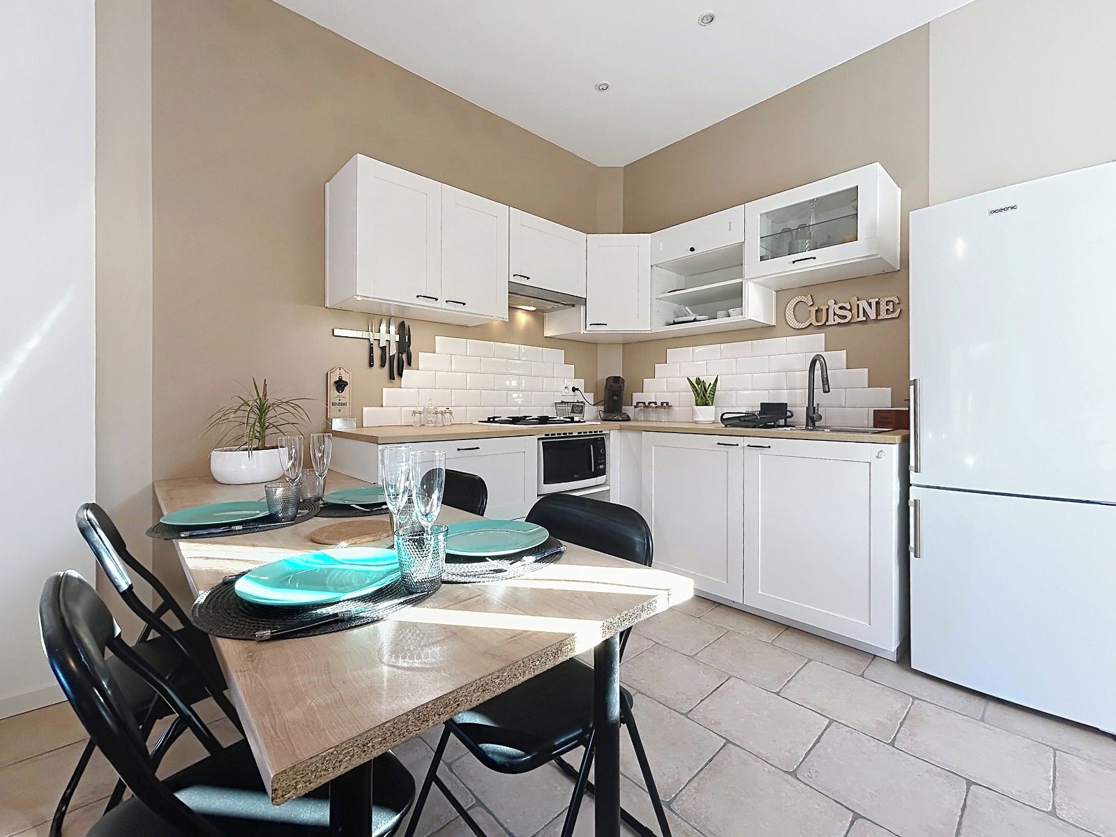 A modern kitchen with white cabinetry, a dining table set with plates and glasses, and a refrigerator.