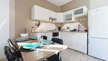 A modern kitchen with white cabinetry, a dining table set with plates and glasses, and a refrigerator.