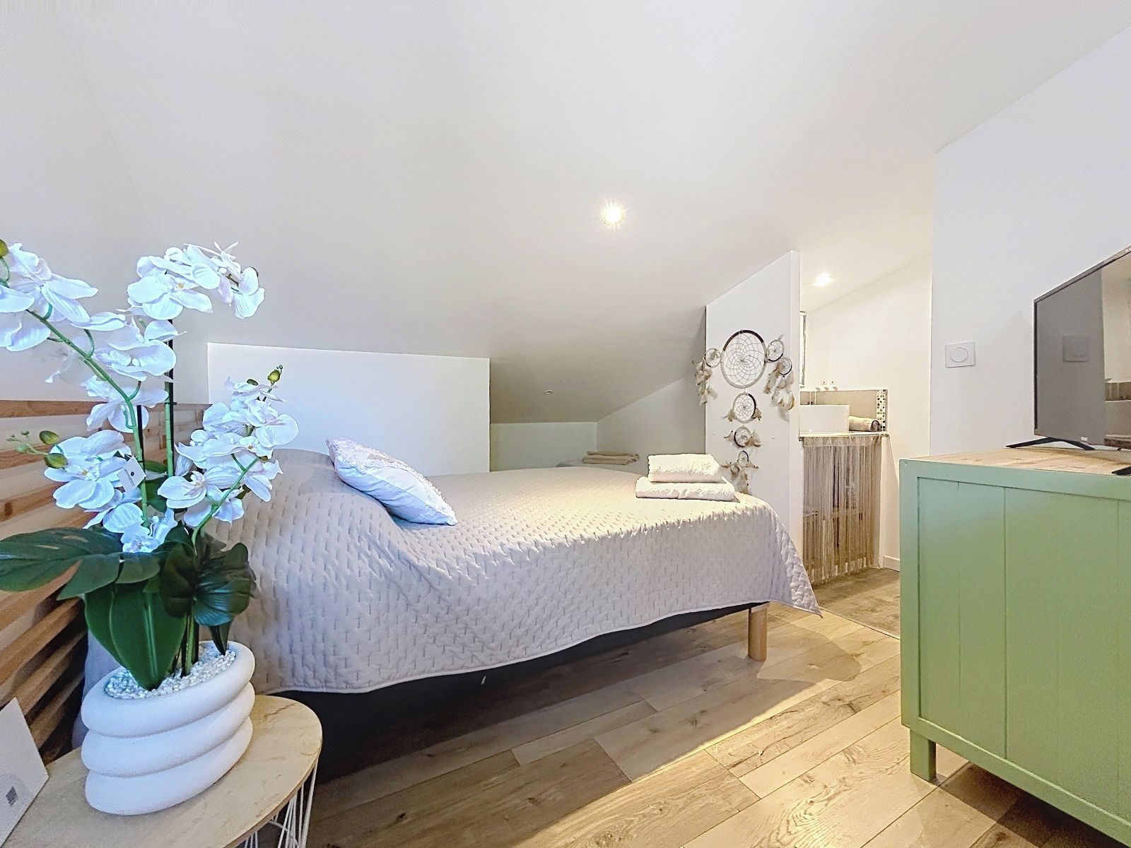 Ein Schlafzimmer mit einem Bett, einem Nachttisch, einem grünen Schrank und einer Wand mit einer Traumfänger-Dekoration.