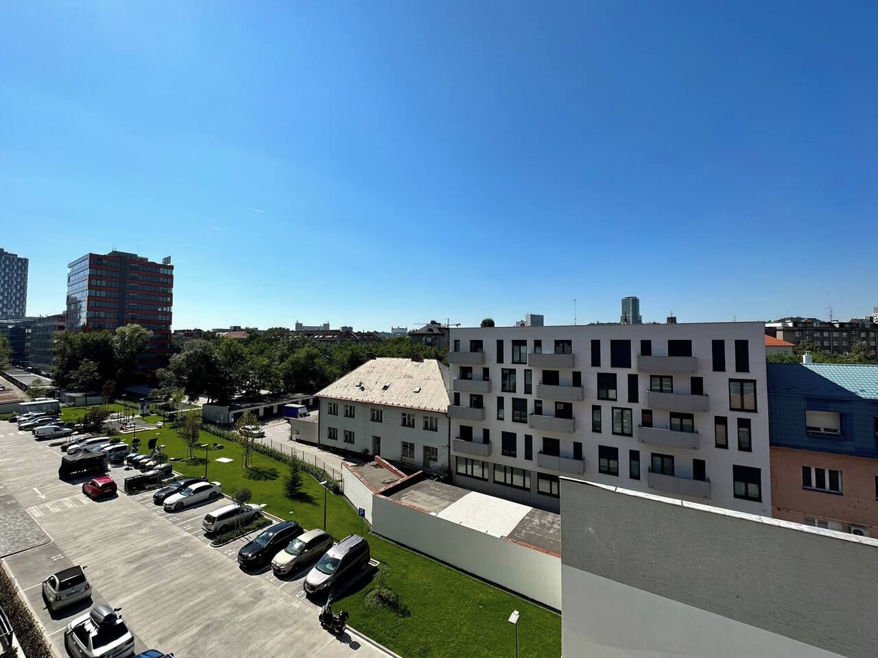 A parking lot with multiple cars, a building with a flat roof, and a clear blue sky.
