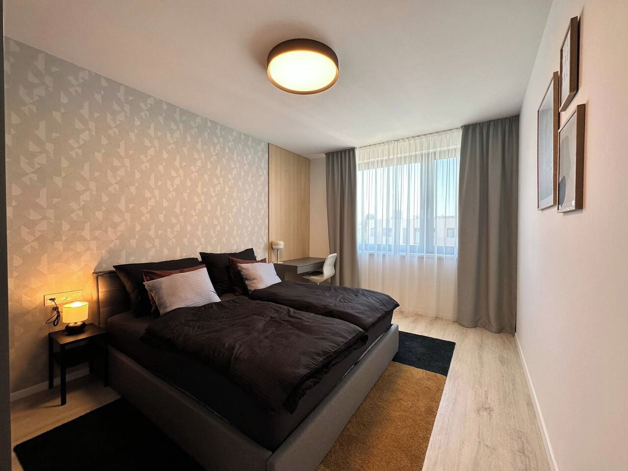 Habitación de hotel con cama doble, mesitas de noche, escritorio y un ventanal con cortinas.