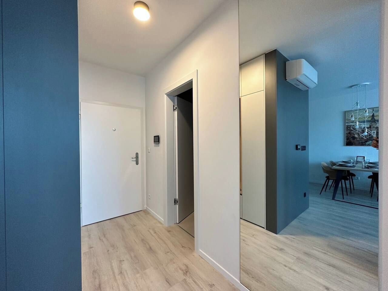 A hallway with a door, a small room, and a dining area with chairs and a table.